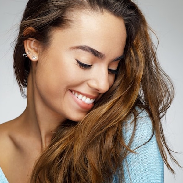 A woman with long brown hair looking down with a perfect smile thanks to cosmetic veneers