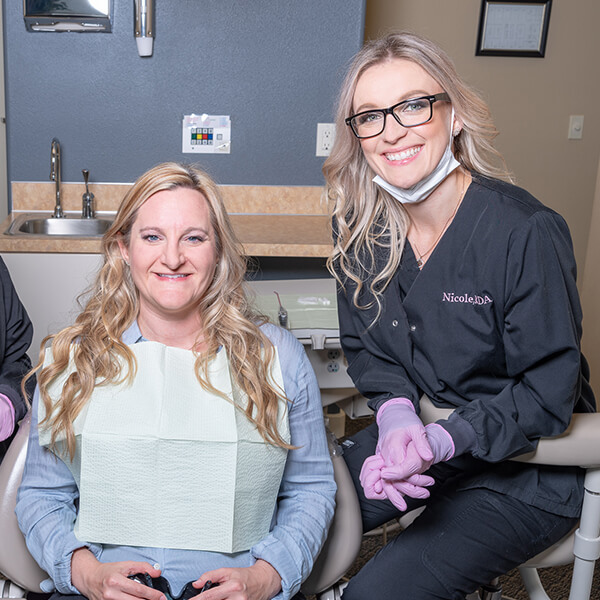 One of our dental hygienists, Nicole, smiling with a patient in a dental chair