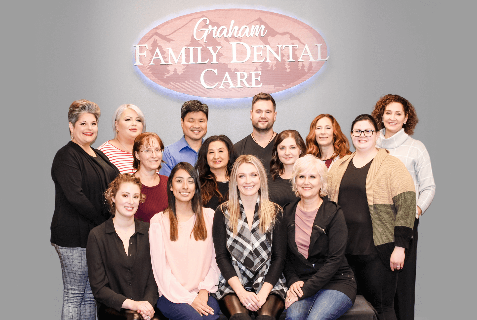 The entire Graham Family Dental Care team standing together under our logo in the office